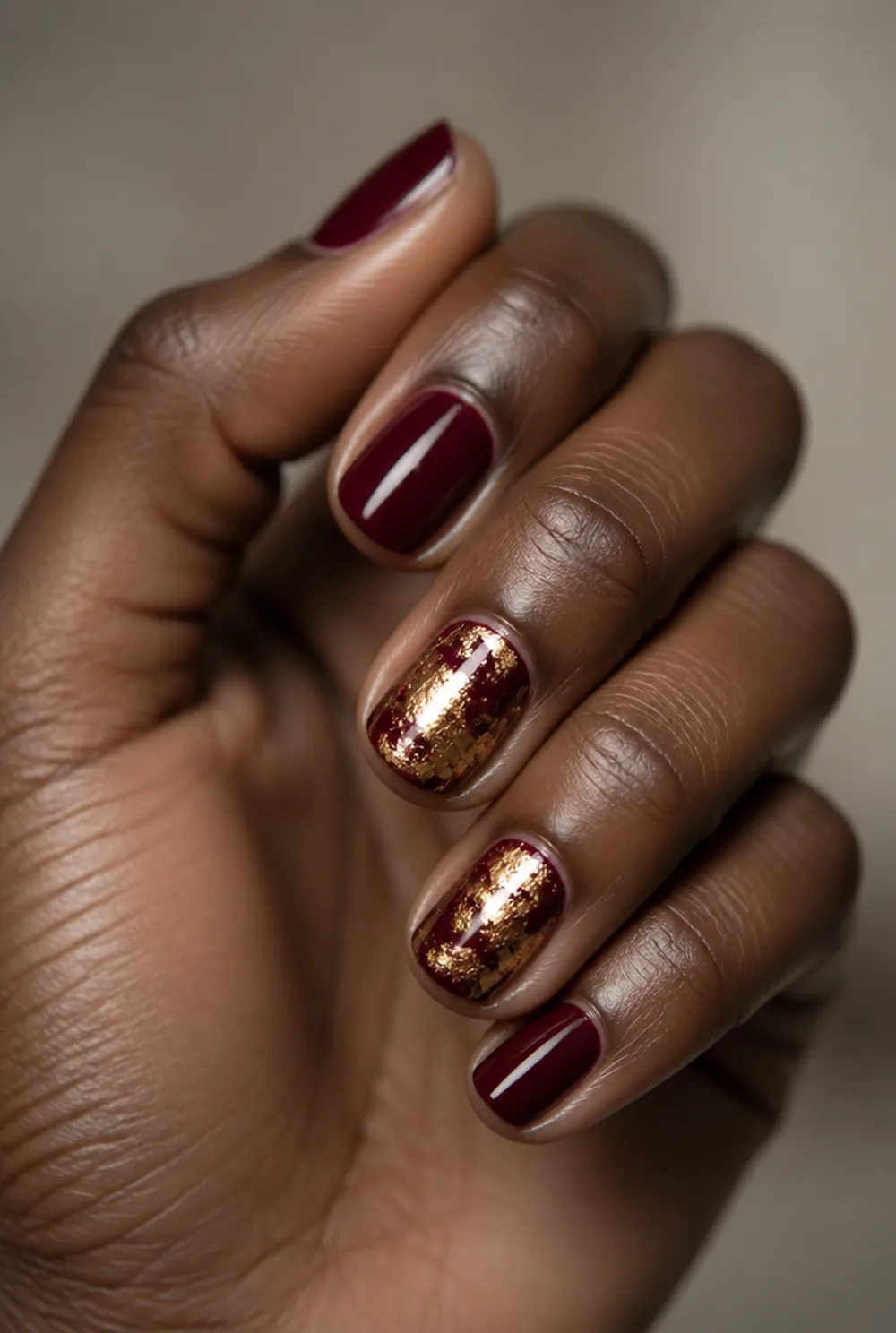 gold and burgundy nail art on deep brown skin
