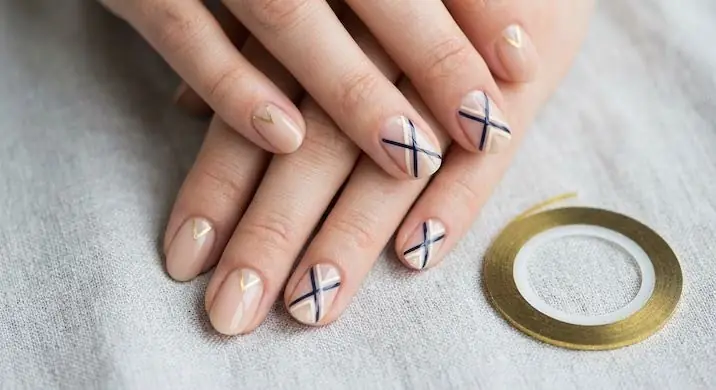 GeometricPatterns - PolishedAndPrettyNails.com Geometric nail design with thin black crossed lines on nude nails beside gold striping tape
