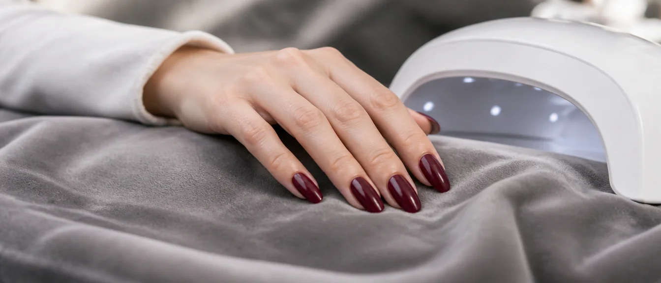 A glossy rich burgundy gel manicure on medium almond nails, beside a compact white LED nai - PolishedAndPrettyNails.com A glossy rich burgundy gel manicure on medium almond nails, beside a compact white LED nail lamp