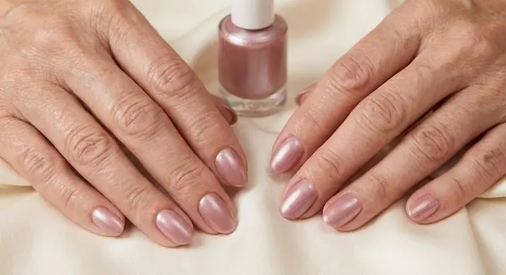 Pearl-Finish Elegance - PolishedAndPrettyNails.com Pearl-finish nails in shimmering soft pink on mature hands beside a bottle of polish