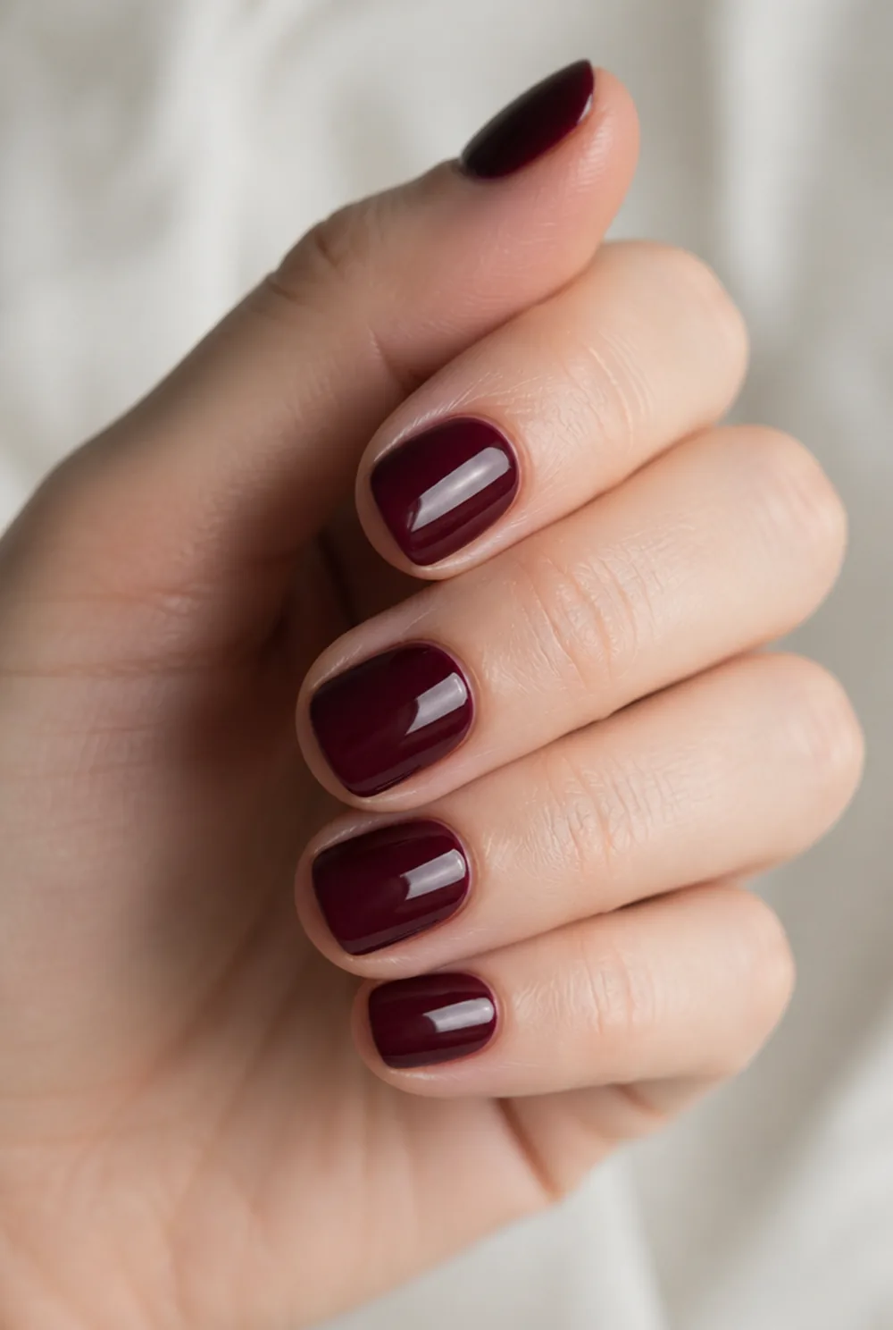 round burgundy nail art on fair skin, short length