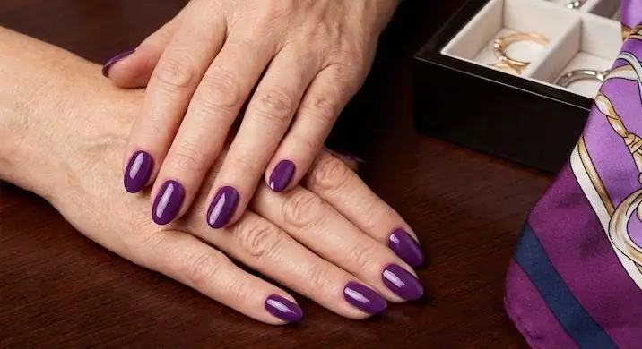 Timeless Deep Jewel Tones - PolishedAndPrettyNails.com Deep jewel-tone purple nails on mature hands resting on a silk scarf