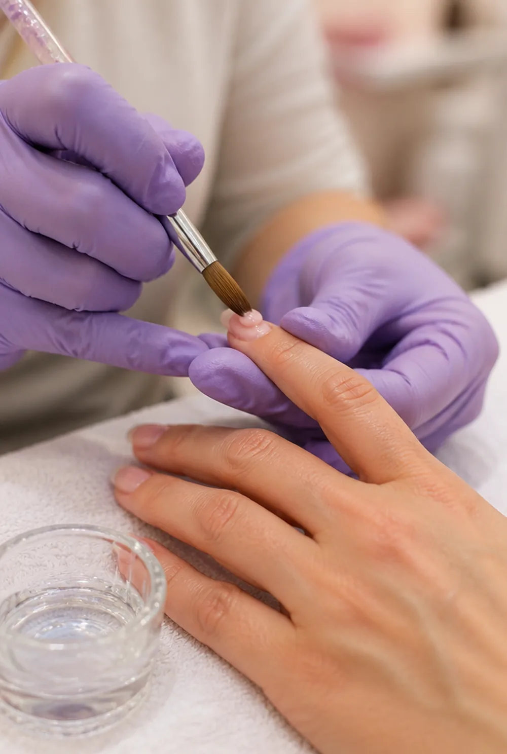 Acrylic bead application - PolishedAndPrettyNails.com Nail technician in nitrile gloves placing a bead of pink acrylic on a natural nail with a brush